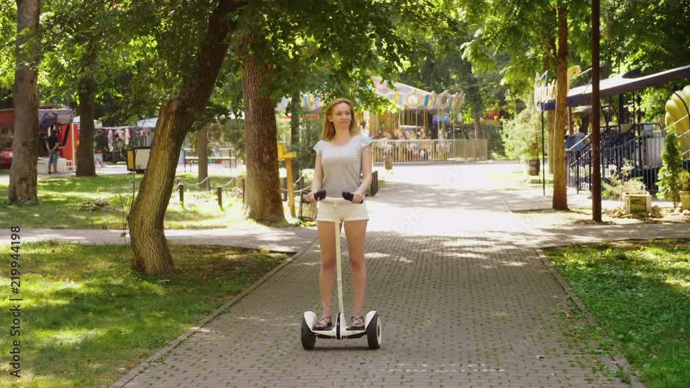 Girl in white shorts, riding a Segway on a clear sunny day. summer park and sun glare. 4k, slow-motion shooting, stadikam shot