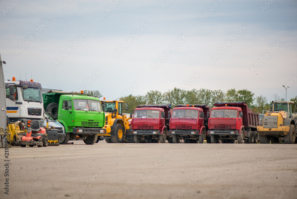 Fototapeta premium Multiple cars, excavators, trucks, loaders, concrete mixers and construction machinery in large parking lot in industrial territory, next to concrete and asphalt factory 