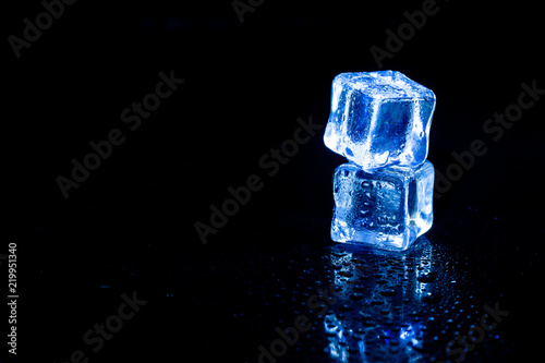 Blue ice cubes reflection on black table background. © peterkai