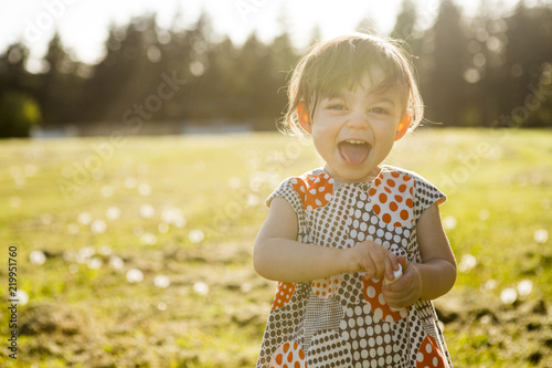 Cute portrait of a little girl in a dress playing in the grass at sunset.