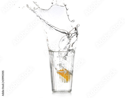 Glass with splashing water and sliced citrus fruit on white background