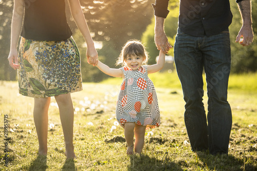 Little girl wearing a dress gets a swing from her parents while holding their hands. photo
