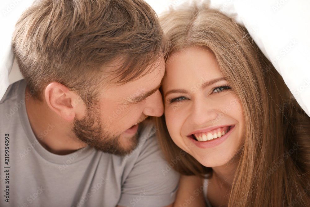 Happy young couple together under blanket in bed at home