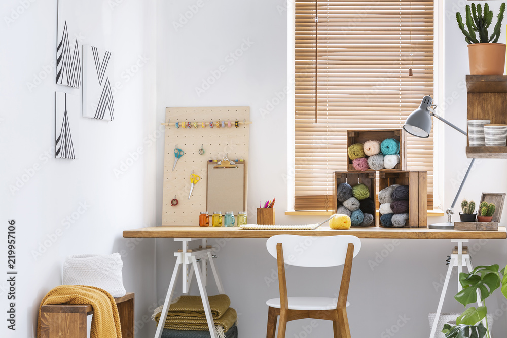 Creative workspace with scandinavian, wooden furniture, white walls and sewing tools in a modern crafts room interior. Real photo. - obrazy, fototapety, plakaty 
