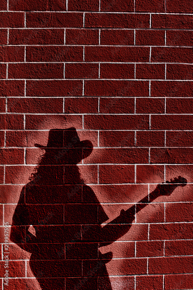 Obraz premium Shadow of musician whit guitar on brick wall 