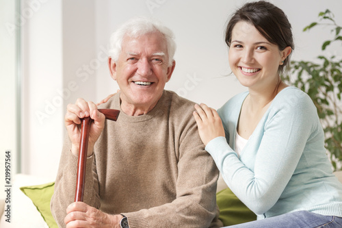Smiling woman hugging happy senior man with walking stick during family meeting