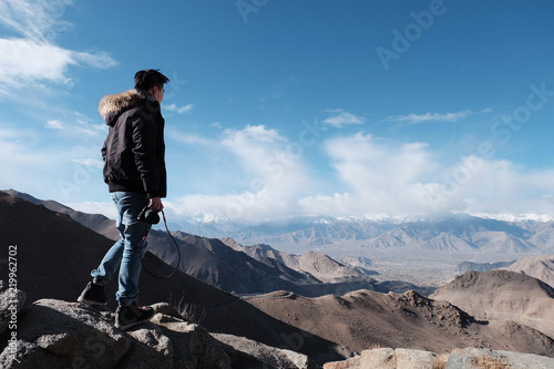 young traveler men with canera at top of the mountain a breathtaking landscape Leh, Ladakh, North India, wanderlust travel concept, space for text, atmospheric epic moment © supakit