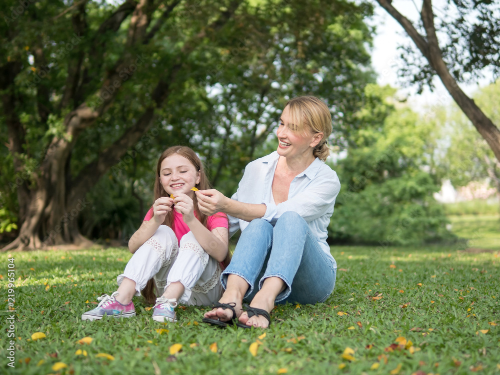 Mother and daughter sitting and playing together in the park. Happy family resting together on green grass. Happy family concept. Mother and daughter sitting and playing together in the park. Happy family resting together on green grass. Happy family concept.