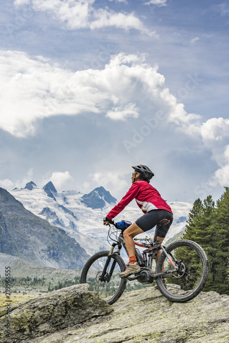 Fototapeta Naklejka Na Ścianę i Meble -  active senior woman, riding her e-mountain bike in the Roseg valley below the glaciers and summits of the Sella Group and Piz Roseg