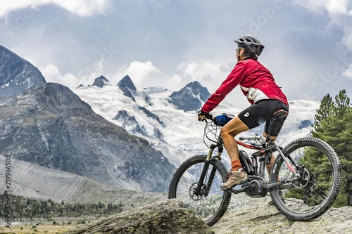 Obraz aktywna starsza kobieta, jeżdżąca na rowerze górskim w dolinie Roseg poniżej lodowców i szczytów Grupy Sella i Piz Roseg