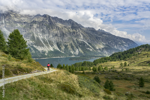 Senior woman, riding here e-mountain bike on the famous trails around the lakes in the upper Engadin, between Saint Moritz and Maloja, Engadin, Switzerland with stunning views on the lake of Silvaplan photo