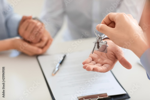 Real estate agent giving key from new house to happy couple in office, closeup