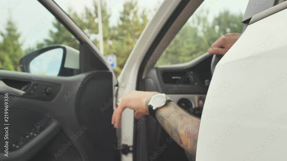 A brutal man with tattoos on his hands opens the door and emerges from his white car. A brutal man with tattoos on his hands opens the door and emerges from his white car.