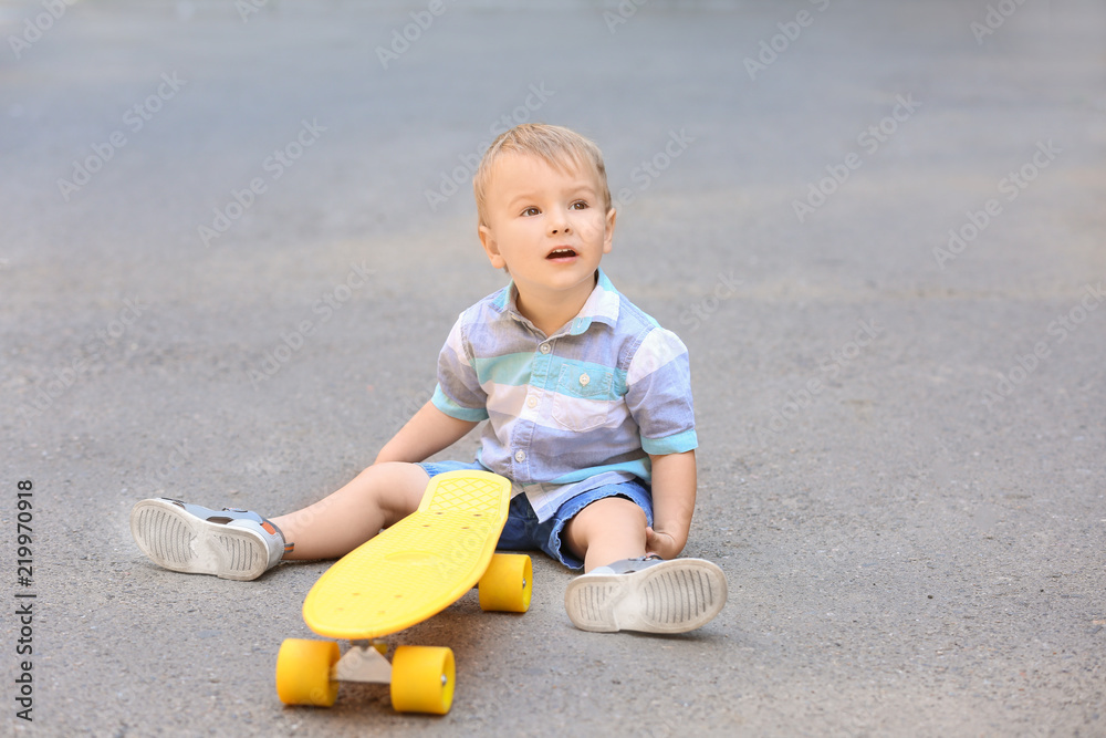 Cute little boy with skateboard sitting on ground outdoors Cute little boy with skateboard sitting on ground outdoors