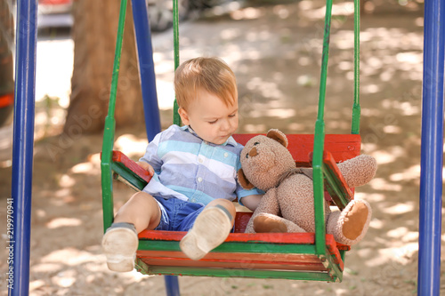 Cute little boy with teddy bear playing on swings outdoors