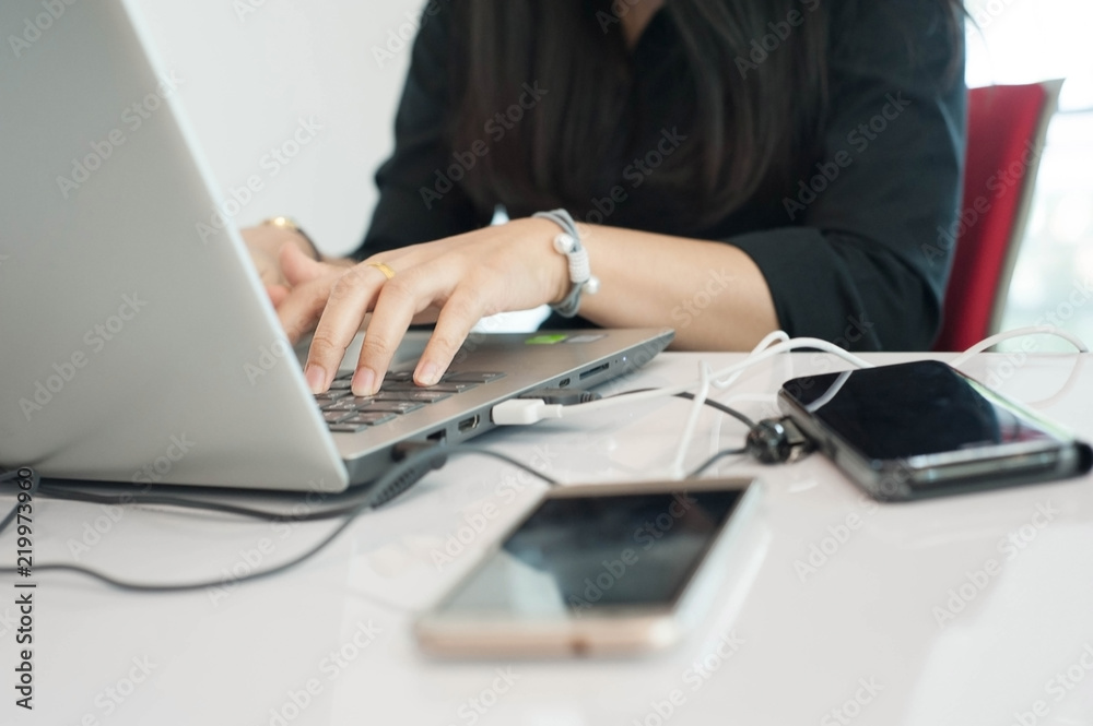 Black shirt women is clicking mouse,Women using hand press keyboard and charging smartphone with USB cable conect to computer,selective focus Black shirt women is clicking mouse,Women using hand press keyboard and charging smartphone with USB cable conect to computer,selective focus