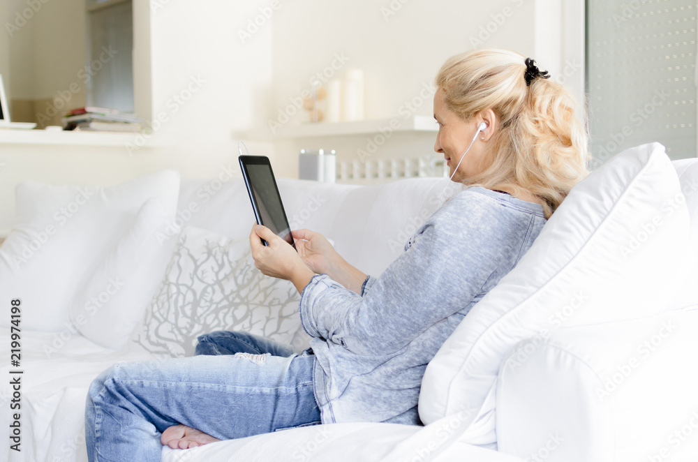 Adult woman sitting on sofa with tablet in hands