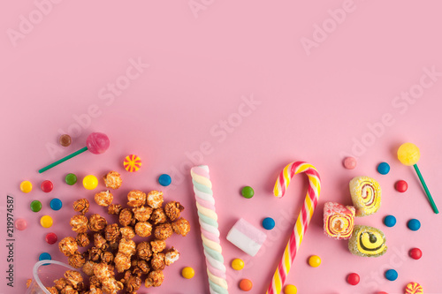 Colored, different sweets, lollipops, marshmallows, caramel popcorn on a pink background. Copy space. Top view