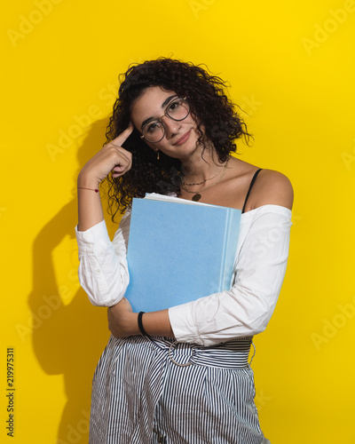 Curly woman posing with book on yellow background