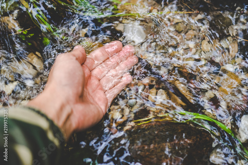 Man hand touching clean, pure, cold water stream photo