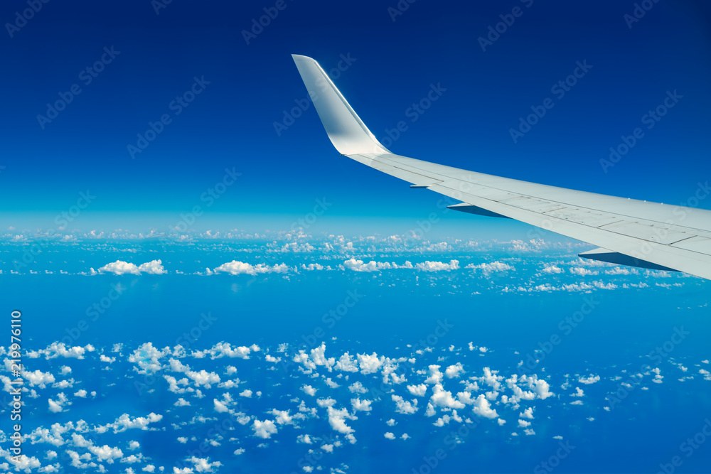 Looking through aircraft window during flight. Aircraft wing over blue skies and white clouds.Copy space. Looking through aircraft window during flight. Aircraft wing over blue skies and white clouds.Copy space.