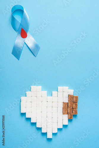 blue ribbon awareness with red blood drop and heart made of sugar cubes on a blue background, world diabetes day