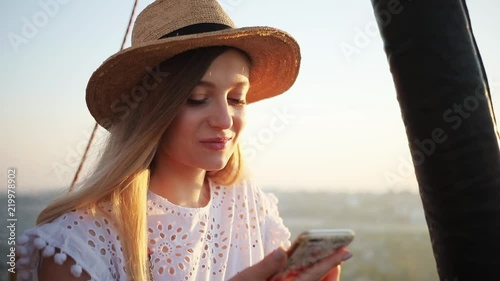 Portrait happy young woman with hat on hot air balloon use phone smile sunset sunrise sky freedom morning nature view flight hot basket tourists couple adventure airship high close up slow motion