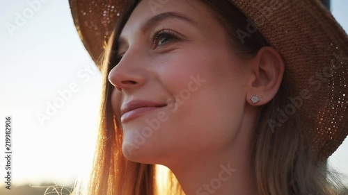 Close up of woman's face with hat smile feel happy outside at sunrise sunset beautiful girl lifestyle nature people summer eyes portrait background beach outdoor relax sunlight portrait slow motion