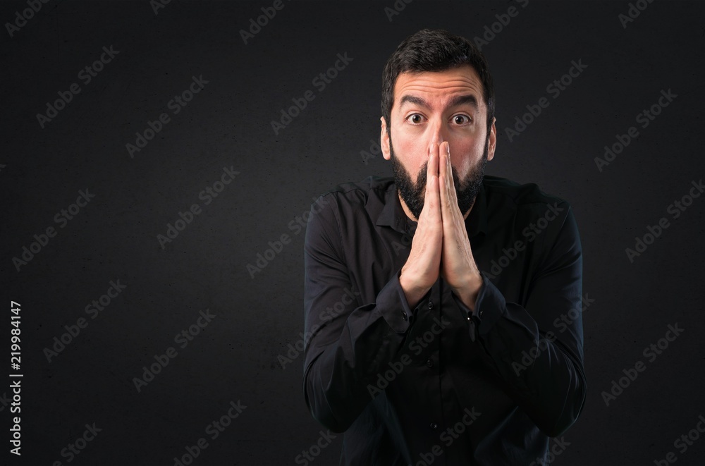 Handsome man with beard pleading on black background Handsome man with beard pleading on black background