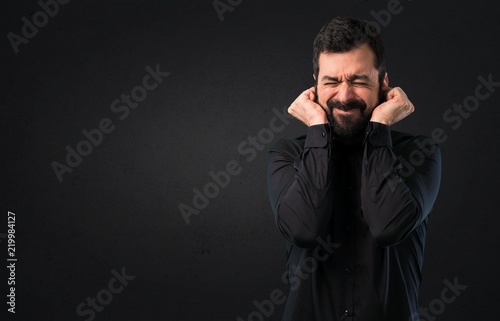 Handsome man with beard covering his ears on black background