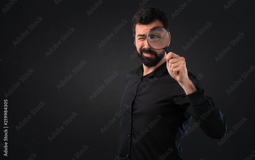 Obraz premium Handsome man with beard with magnifying glass on black background