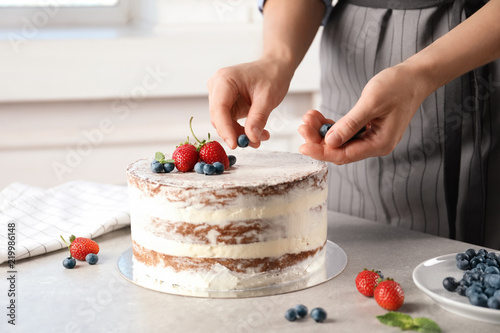 Woman decorating delicious cake with fresh berries at table. Homemade pastry