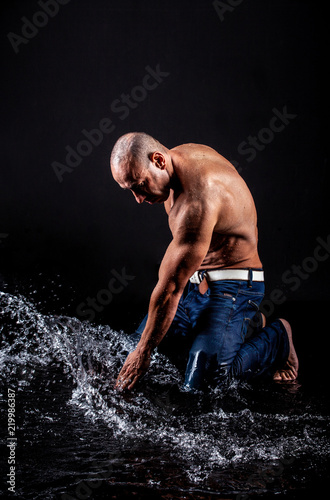 very muscular handsome athletic man striking with a hand on water