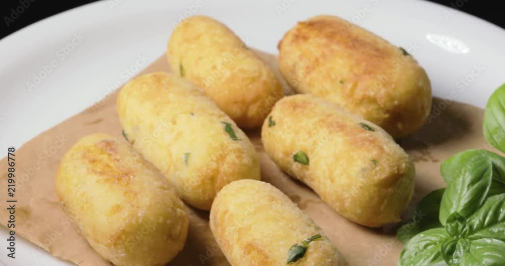 Crocchette di patate infarinate con prezzemolo disposte su un piatto bianco rotante con basilico e formaggio grattugiato. Dieta vegetariana e vegana. Crocchette di patate infarinate con prezzemolo disposte su un piatto bianco rotante con basilico e formaggio grattugiato. Dieta vegetariana e vegana.