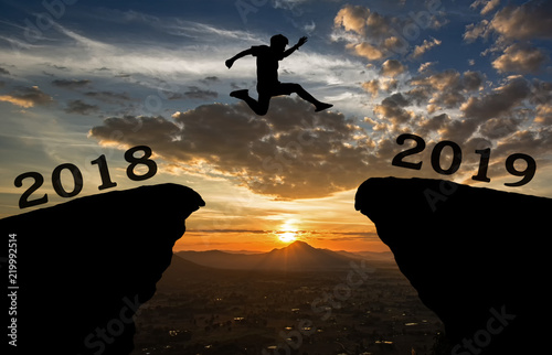 A young man jump between 2018 and 2019 years over the sun and through on the gap of hill  silhouette evening colorful sky. happy new year 2019.