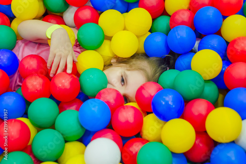 happy little girl having fun in ball pit with colorful balls. © NATALYA