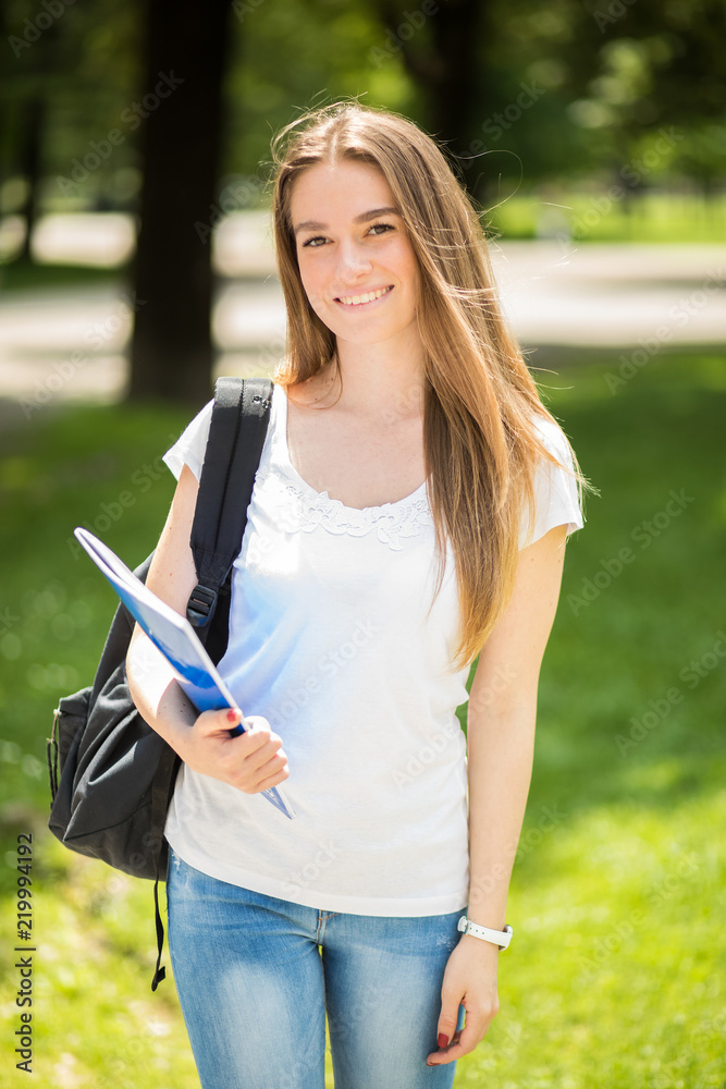 Female student holding a book outdoor in the park and smiling Female student holding a book outdoor in the park and smiling