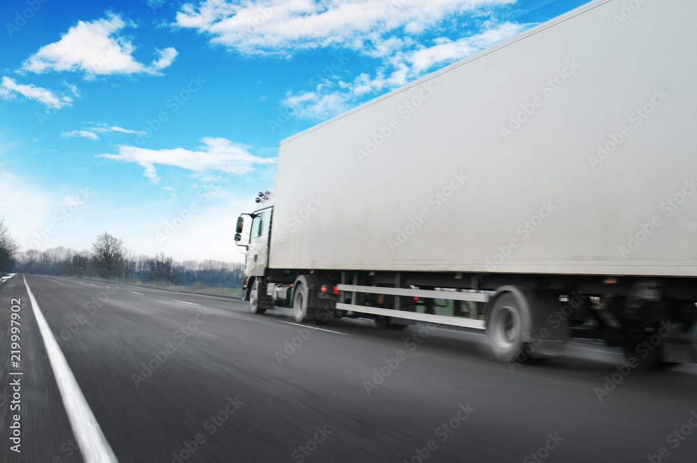 Truck driving fast with a trailer on the countryside road against sky