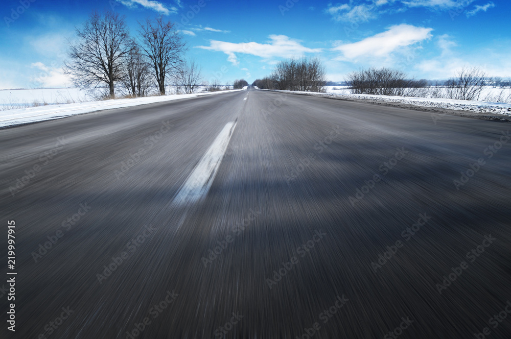 Winter countryside road in motion with snow against blue sky with clouds