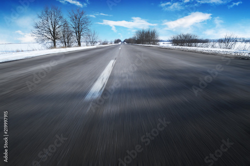 Winter countryside road in motion with snow against blue sky with clouds