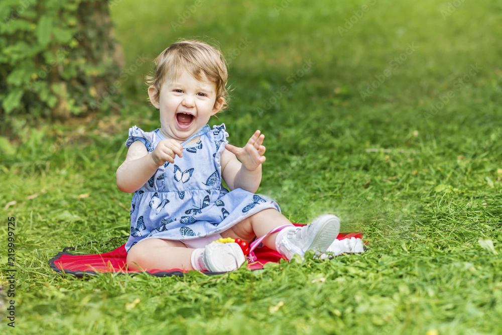 Happy Cute Baby Girl Sitting in the Summer Park and Laughing Happy Cute Baby Girl Sitting in the Summer Park and Laughing