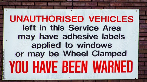 Vehicle wheel clamping warning sign attached to a brick wall.