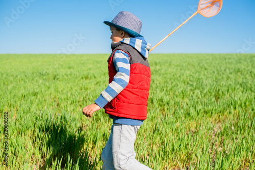 Little boy with a butterfly net in hand runs across the green field. photo