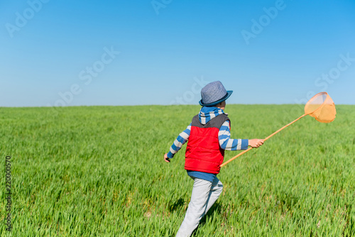 Little boy with a butterfly net in hand runs across the green field. photo