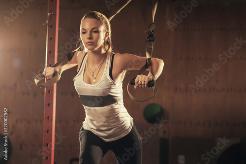 Woman athlete doing exercise in gym. Young attractive girl exercising with suspension trainer. Sportswoman working out in functional training. Workout. Sports.