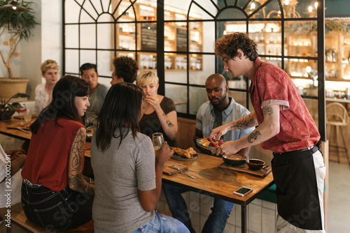 Waiter serving freshly made food to smiling bistro customers