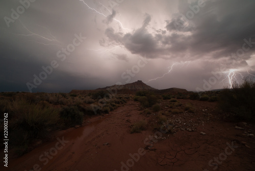 One bolt of lightning strikes in the distance while another zigzags across the sky lighting the desert below Gooseberry Mesa in Southern Utah. 