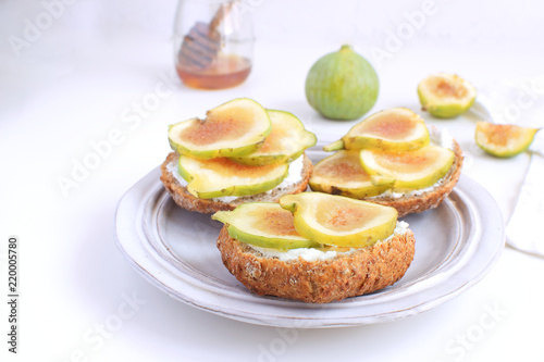 Fresh green figs Porcelain plate Wholegrain bread Honey Goat cheese Healthy eating concept Canapes Sandwiches Appetizer Copy space White background