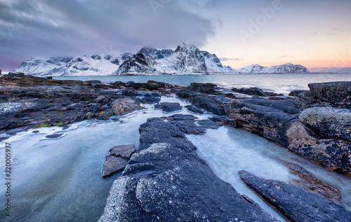 Seashore with stones and ice during sunset. Beautiful natural seascape in the Lofoten islands, Norway. Sea and mountains at the winter