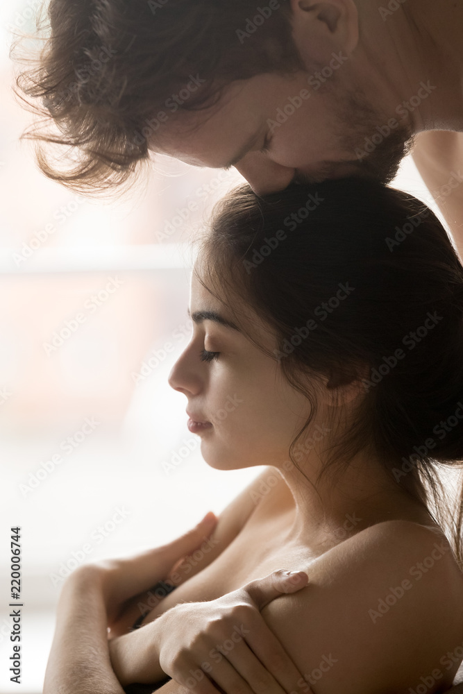 Passionate boyfriend kiss girlfriend head during romantic foreplay in bedroom, couple enjoy tender prelude before love making, young woman undress while lover caressing her before sex, close up view Stock Photo 
